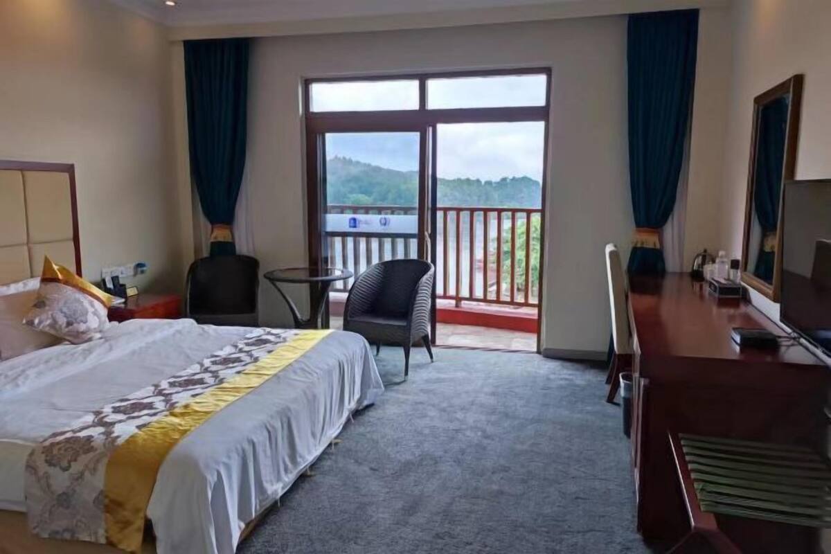 A hotel room with a bed, a desk, a chair, and a balcony with a view.