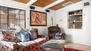 Een woonkamer met een gestreept sofa, een bruine leren fauteuil, een glazen salontafel en een rood vloerkleed.