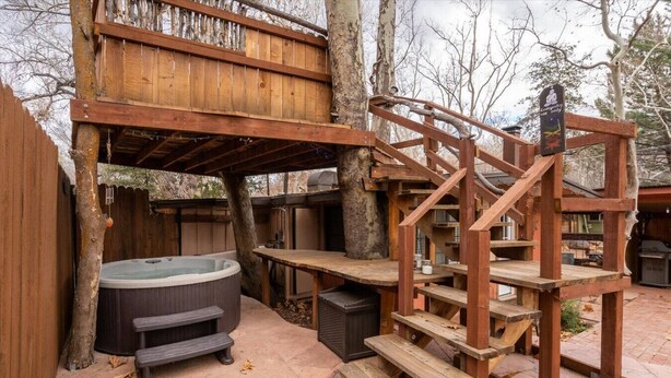 Een houten terras met een jacuzzi, picknicktafels en een houten trap.