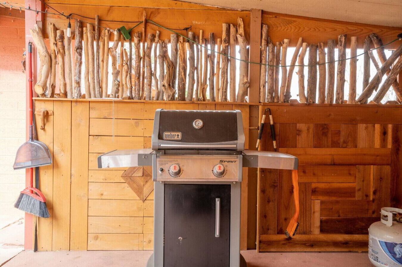 Ein Weber Spirit tragbarer Gasgrill mit Propangasflasche davor, vor einer rustikalen Holzwand.