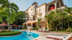 A resort with a swimming pool, lounge chairs, and a large building with balconies. - Gorgeous Balaji Palace with Private Beach (Río San Juan)