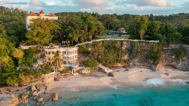 A coastal resort with a large building featuring multiple balconies and a red-roofed structure. - Gorgeous Balaji Palace with Private Beach (Río San Juan)
