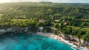 An aerial view of a coastal property with a beach, lush greenery, and a cliff overlooking turquoise waters. - Gorgeous Balaji Palace with Private Beach (Río San Juan)