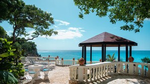 A gazebo with a stone floor and white railing, overlooking a beach with clear blue water. - Gorgeous Balaji Palace with Private Beach (Río San Juan)