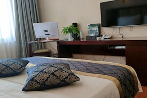 Una habitación de hotel con una cama, un escritorio con computadora, un televisor y una planta.