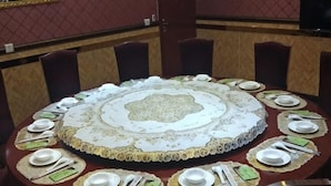 A round table with a lace tablecloth, surrounded by chairs and set with plates, cutlery, and napkins.