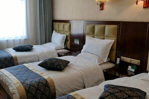 Habitación de hotel con tres camas, cada una con cabecera, almohadas y mesita de noche con lámpara.