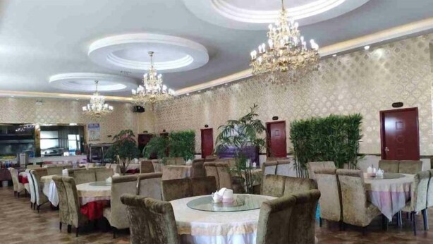 A restaurant with round tables and chairs, chandeliers, and patterned wallpaper.