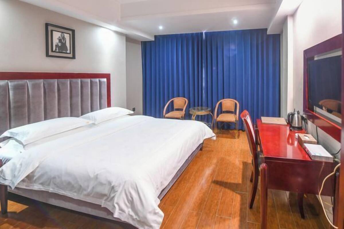 Una habitación de hotel con una cama grande, dos sillas, una mesita, un televisor y una cortina azul.
