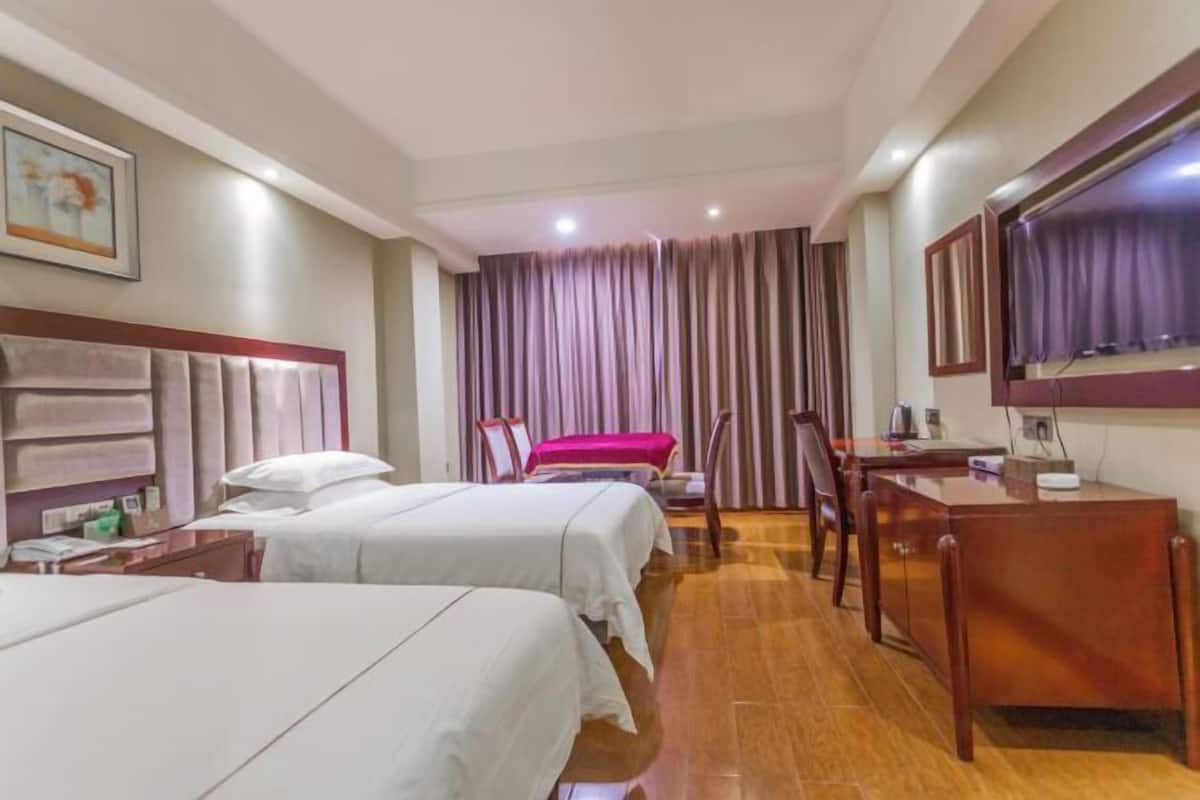 Habitación de hotel con dos camas, un escritorio, una silla, un televisor y una ventana con cortinas.