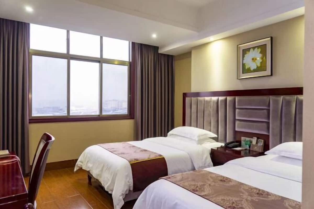 Una habitación de hotel con dos camas, un ventanal grande, una silla y una mesita de noche con un teléfono.