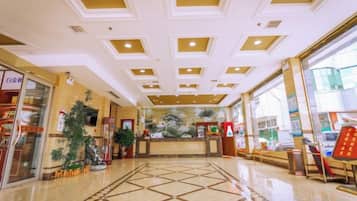 A hotel lobby with a reception desk, a large decorative plant, and a patterned floor.