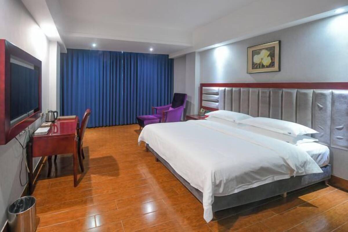 Habitación de hotel con cama, escritorio, silla, televisor y un cuadro en la pared.