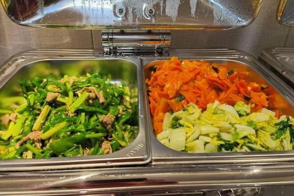 A buffet with two sections: one with green vegetables and meat, and another with shredded carrots and cabbage.