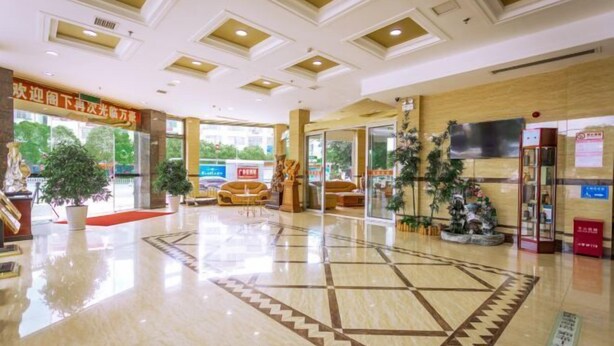 A hotel lobby with a polished marble floor, a reception desk, and potted plants.