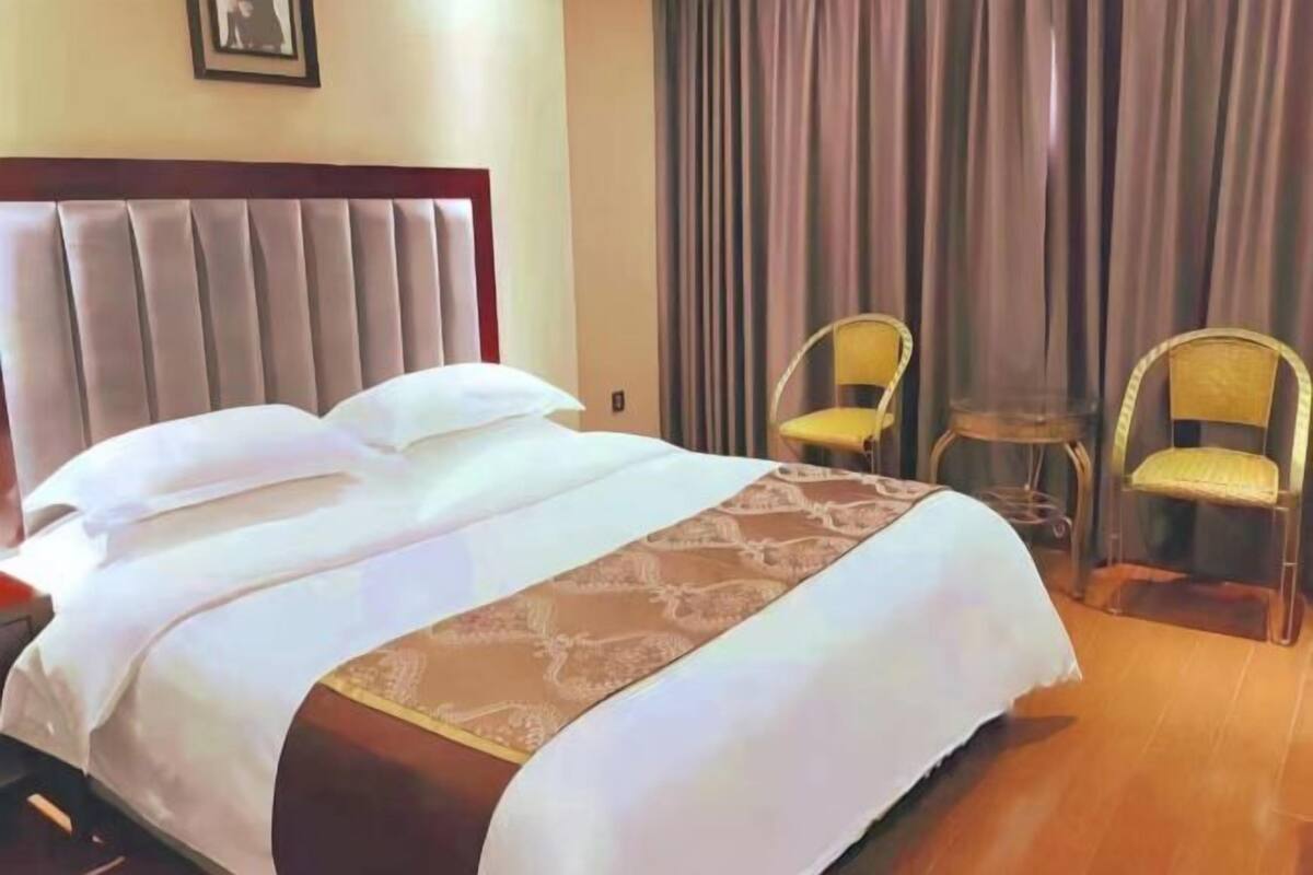 Una habitación de hotel con una cama, dos sillas, una mesita y una cortina.