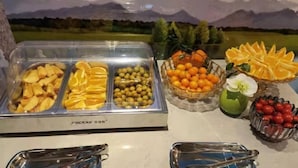 A buffet with various fruits and vegetables, including apples, oranges, and tomatoes, with a scenic mountain backdrop.