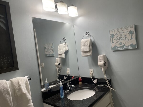 Un baño con lavamanos, dos secadores de pelo, toallero y espejo.