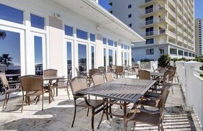 Ein Patio im Freien mit Tischen und Stühlen, großen Fenstern und Blick auf ein Hochhaus.