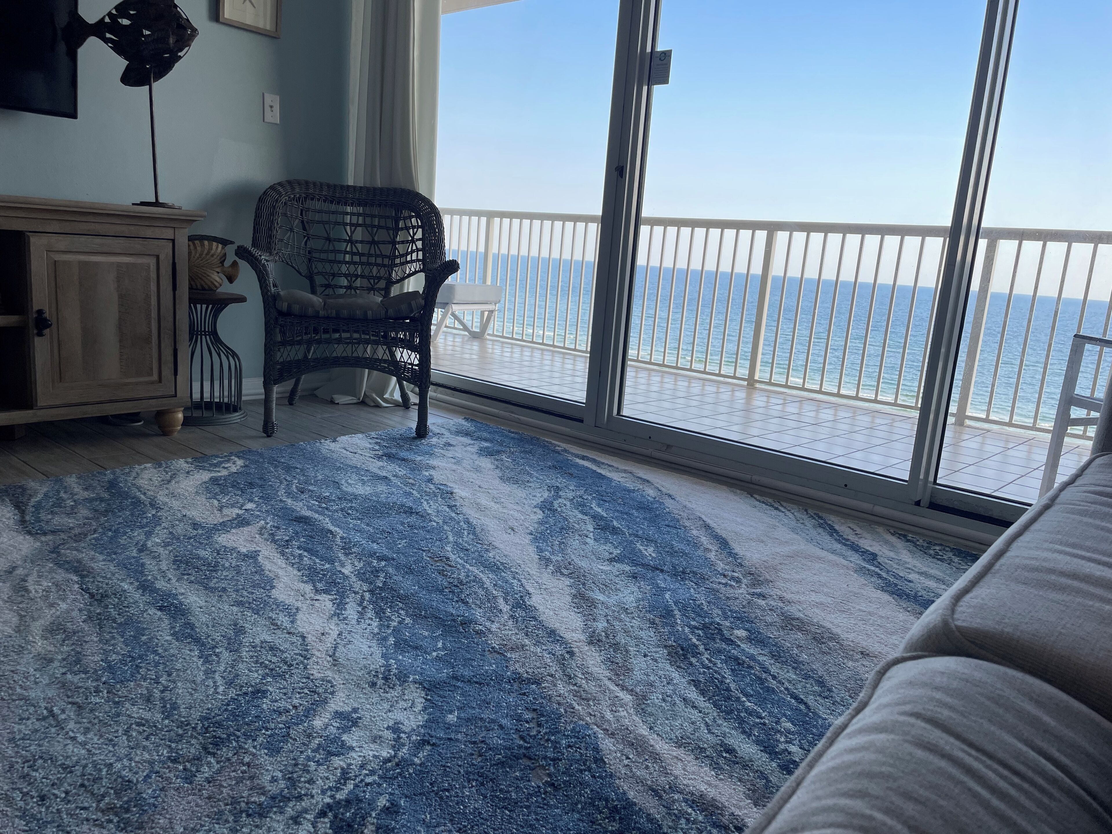 Ein Zimmer mit Meerblick, ein Korbstuhl, ein blaues, gemustertes Teppich und ein Holzkabinett.