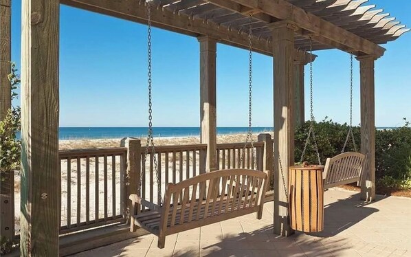 Relax on the beach with a serene view from this pergola, featuring a seating area with benches and a table.