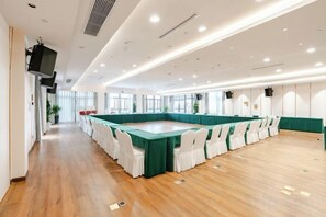 Een grote vergaderzaal met een lange tafel, witte stoelen en een groene tafelkleed.