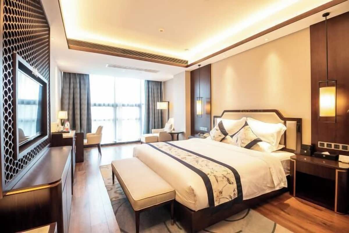 A modern hotel room with a large bed, a desk, a chair, and a TV.