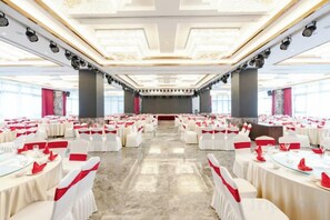 Un salón de banquetes con mesas redondas, manteles blancos y cintas rojas.