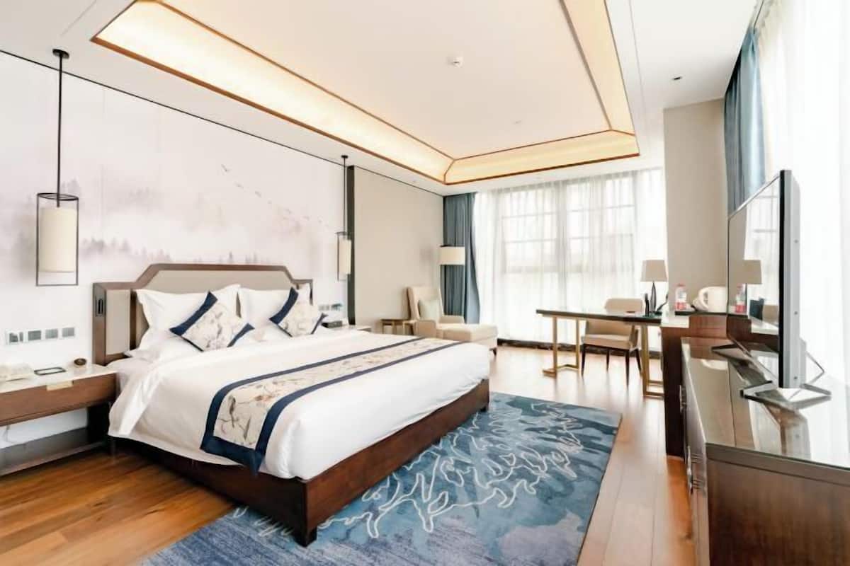 A modern hotel room with a large bed, a desk, and a chair.