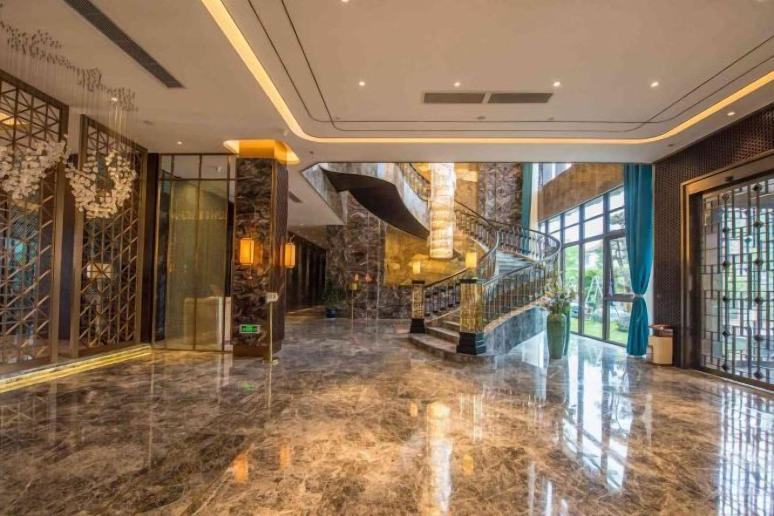 A spacious lobby with a polished marble floor, a grand staircase, and large windows allowing natural light.