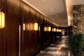 Um corredor longo com painéis de madeira e luminárias fixadas na parede, que leva a uma área de recepção.