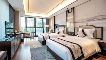 A modern hotel room with two beds, a desk, and a large window offering a view of the outdoors.