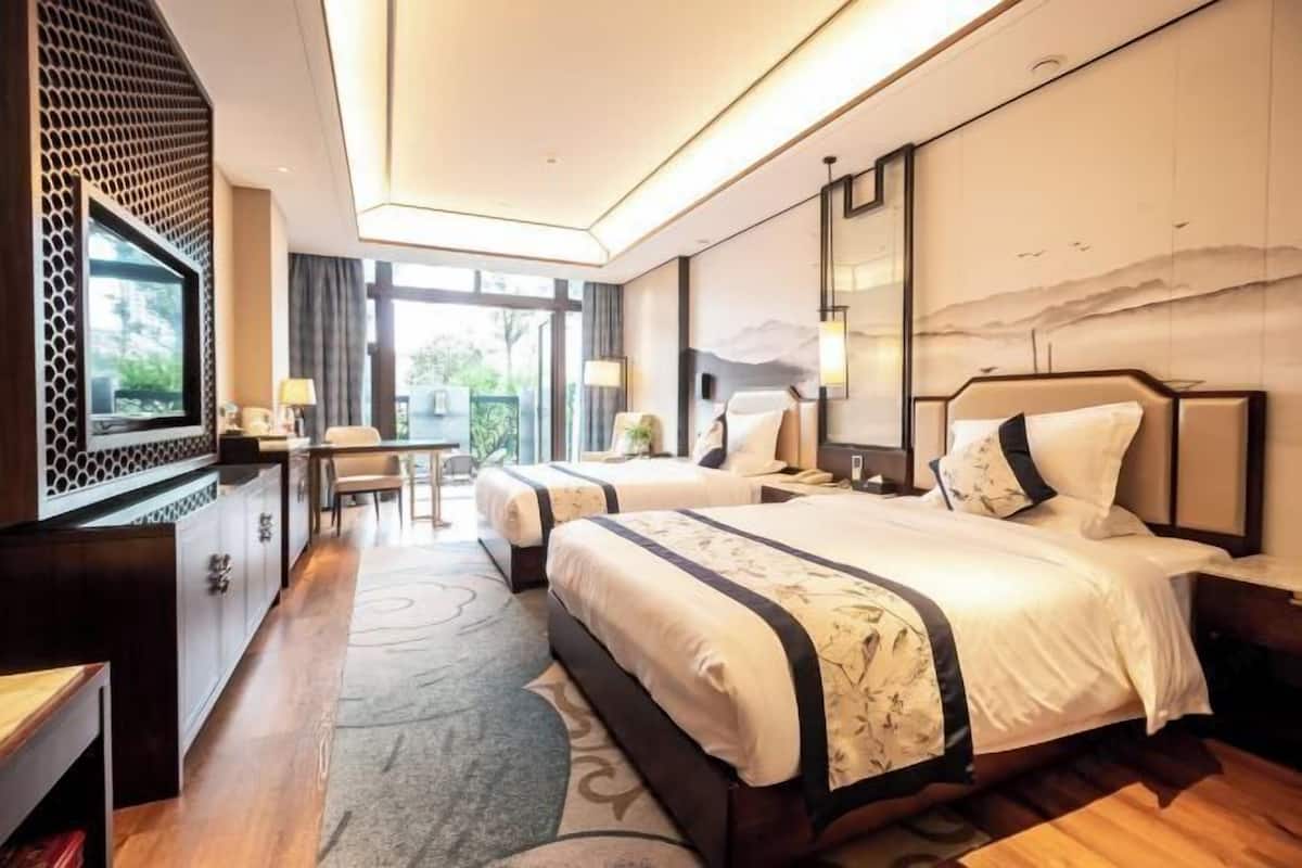 A hotel room with two beds, a desk, a TV, and a large window.