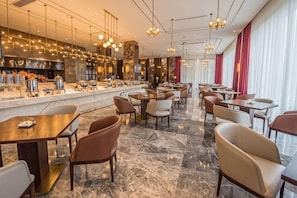 Um restaurante moderno com chão de mármore, diversas mesas e cadeiras para refeições e um bar com vários equipamentos de cozinha.