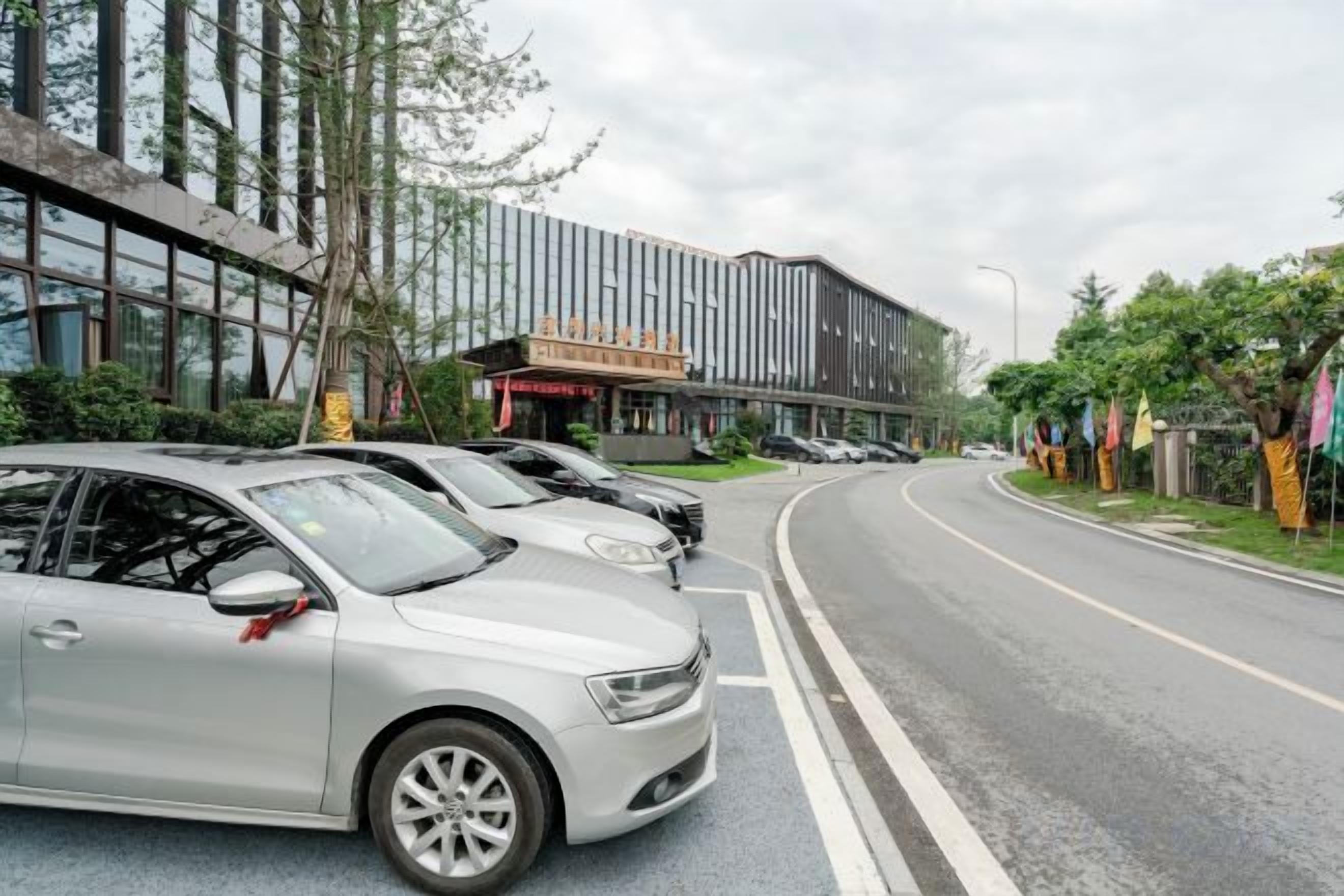Un estacionamiento con varios autos, un edificio moderno con la entrada de un teatro y una carretera curva.