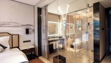 Une chambre d’hôtel moderne dotée d’une douche en verre, d’un lit avec une tête de lit et d’une table de chevet.