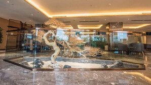 A lobby with a glass enclosure featuring a sculptural tree and rocks, marble flooring, and modern furniture. - Jinyang Shangcheng Hotel (Jintang)