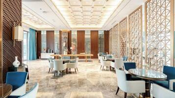 Um amplo saguão de hotel com área de refeições central, diversas opções de assentos e um painel decorativo.