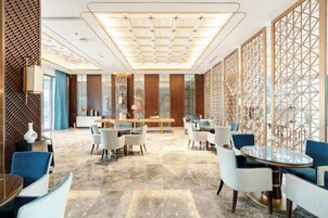 Un amplio hall de hotel con zona de comedor central, varios conjuntos de asientos y un mamparo decorativo.
