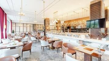 Un restaurante espacioso con numerosas mesas y sillas, una zona de bar y una pantalla grande.