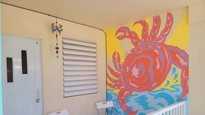 A room with a white door, a window with blinds, a colorful mural of a crab, and two white chairs. - Apt w/ Pool Deck & Games, 5 mins From The Beach- CU (Isabela)