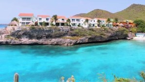 Un hotel frente al mar con varias construcciones, un litoral rocoso y agua turquesa cristalina.