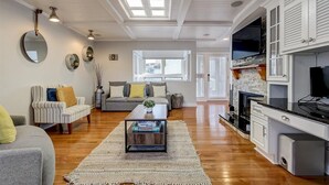 A spacious living room with a fireplace, a kitchen with white cabinetry, and a large window providing natural light.
