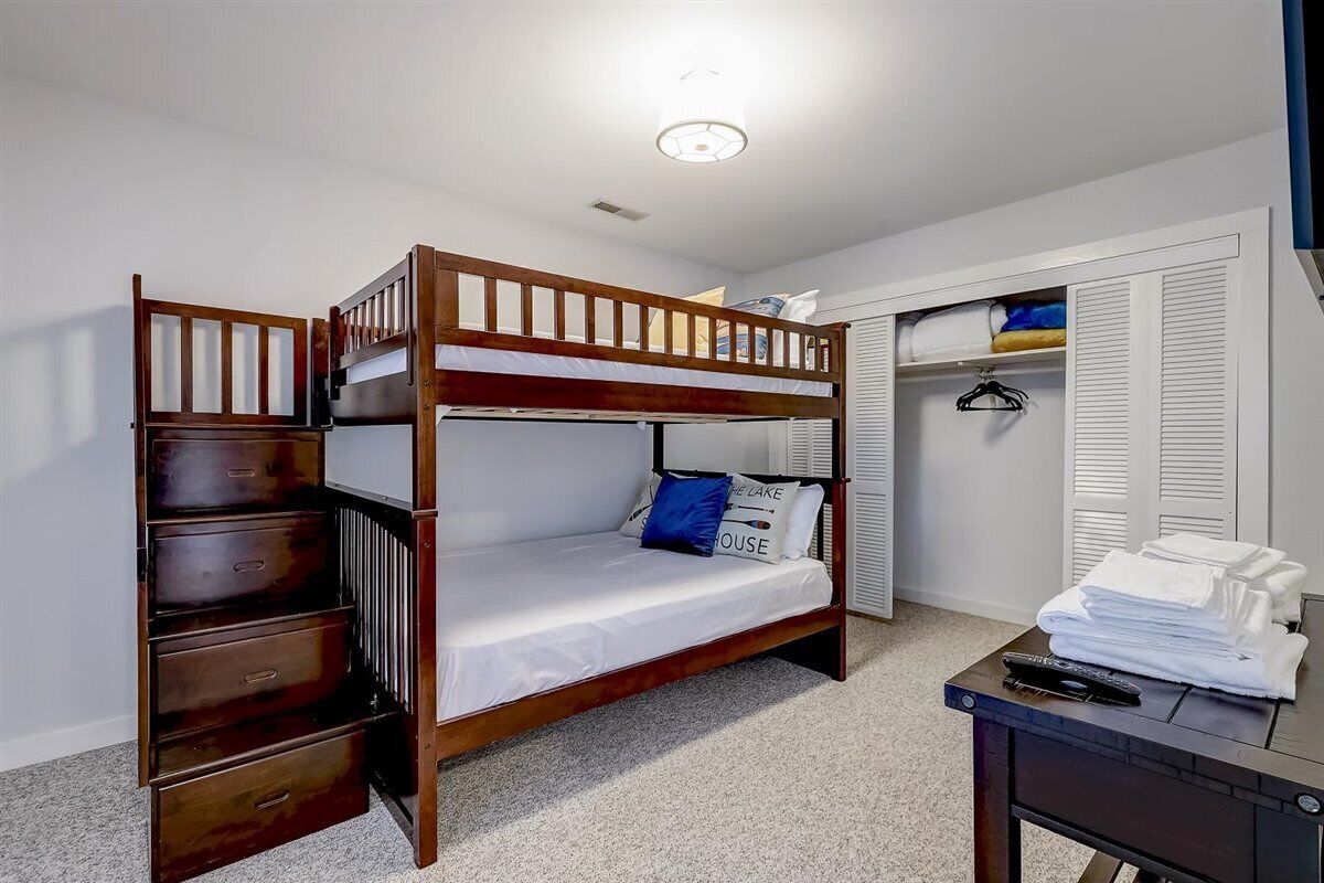 Una cama litera con cajones para guardar objetos, un escritorio con control remoto y un armario con ropa colgada.
