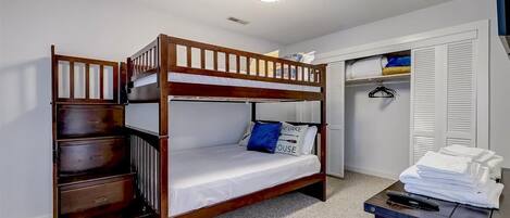 Una cama litera con cajones para guardar objetos, un escritorio con control remoto y un armario con ropa colgada.