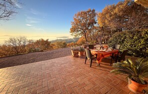 Un espace de restauration en plein air avec une terrasse en briques, une table dressée pour deux personnes et une vue sur la campagne.