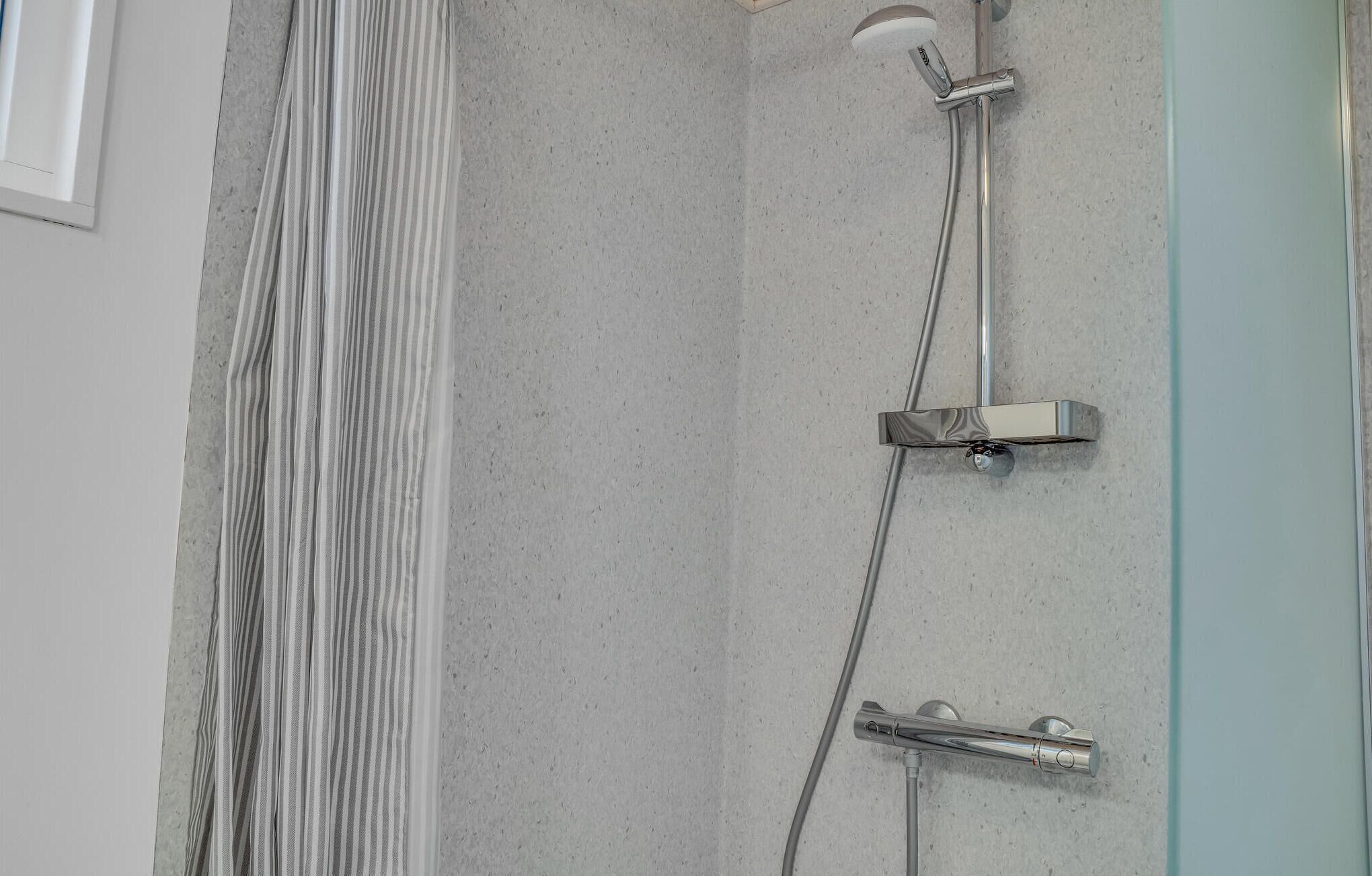 Une douche dotée d’une porte en verre, d’un panneau de commande et d’un pommeau de douche à main.