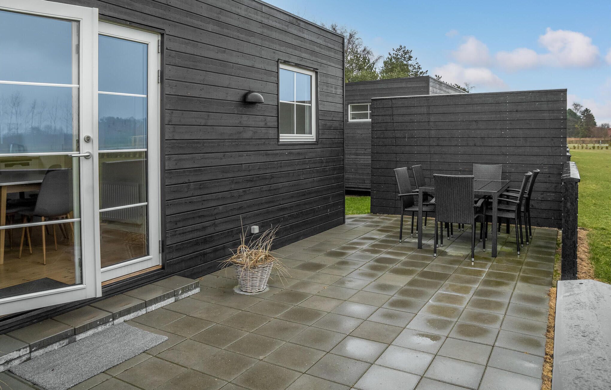 Uma casa moderna com área de varanda, mesa e cadeiras, um pequeno jardim e uma porta de correr de vidro.