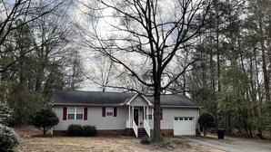 A single-story house with a front porch, a garage, and a yard with leaf-covered ground. - Cozy House Close To Everything Anderson Has To Offer (Anderson)