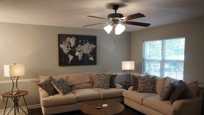 A living room with a beige sectional sofa, two side tables with lamps, a world map on the wall, and a ceiling fan. - Cozy House Close To Everything Anderson Has To Offer (Anderson)